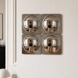 May include: A set of four square wall mirrors arranged in a two-by-two grid. Each mirror features a central circular convex glass surface with a polished metallic frame, creating a reflective, curved distortion of the surrounding room.