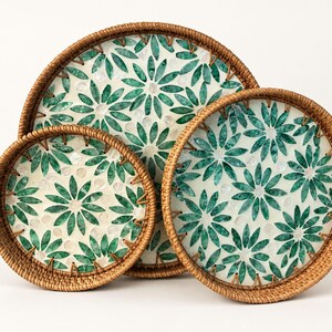 May include: Three round trays with woven brown rattan rims and a white base featuring a repeating green floral petal pattern. The trays are arranged in a cluster, each showing a consistent design of green leaf-like shapes forming flowers.