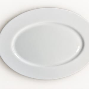 May include: A plain white oval serving platter with a smooth, glossy finish and a wide, flat rim. The dish features a simple, clean design with a shallow center basin, providing a versatile surface for presenting various food items in a dining setting.