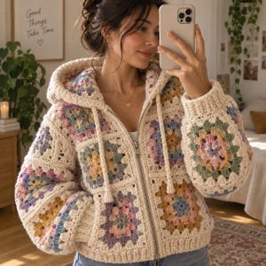 Op de afbeelding: Een vest met rits en capuchon gemaakt van crèmekleurig garen, bestaande uit een patchwork van veelkleurige granny square-motieven in tinten zachtroze, gedempt blauw, saliegroen en mosterdgeel, afgewerkt met een zilverkleurige metalen ritssluiting.