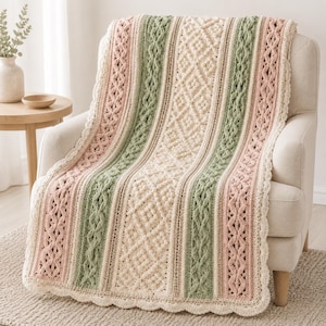 Puede incluir: Una manta de ganchillo rectangular con rayas verticales en color crema, verde salvia y rosa empolvado. El diseño incorpora texturas complejas de estilo trenzado, patrones de diamantes y un borde festoneado en todo el contorno.