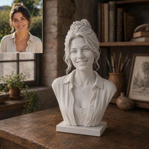 Può includere: Un busto in pietra bianca che raffigura una persona sorridente con i capelli raccolti in uno chignon, che indossa una camicia con colletto e una collana. La scultura è montata su una base rettangolare e riproduce i tratti del viso e l'abbigliamento.