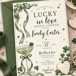 May include: A cream-colored bridal shower invitation featuring green watercolor shamrocks, a ribbon-tied cocktail glass, and gold heart accents. Text reads: Lucky in love, Bridal Shower, Emily Carter, Saturday March 17 2026, The Clover Inn.