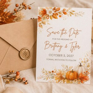 May include: A white rectangular wedding save the date card with autumn leaf and pumpkin illustrations, featuring the text Save the Date for the wedding of Brittany & Tyler October 3, 2027, next to a brown envelope with a gold wax seal.