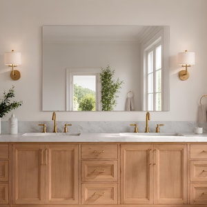 May include: A double vanity cabinet made of light-toned wood with a white marble countertop and two integrated sinks. It features brass faucets, multiple drawers, and cabinet doors with brass hardware, positioned beneath a large rectangular mirror.