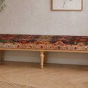 May include: A long rectangular bench featuring a cushioned seat upholstered in a multi-coloured fabric with a detailed floral and geometric pattern. The bench is supported by six light-toned wooden legs with a turned, spindle-style design.