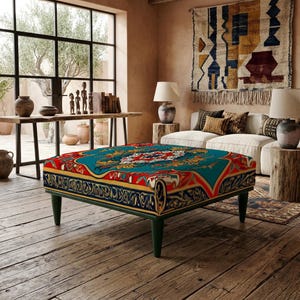 Könnte beinhalten: Ein quadratischer Hocker mit einem lebendigen, mehrfarbigen Muster in den dominierenden Tönen Türkis, Rot und Gold. Der Bezug zeigt ein komplexes, symmetrisches Design mit floralen und geometrischen Motiven. Er steht auf vier dunklen Holzbeinen.