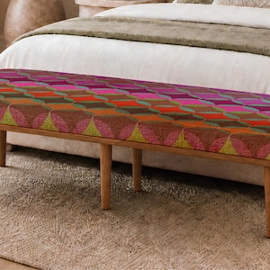 May include: A rectangular bench featuring a cushioned seat upholstered in a vibrant, multi-colored fabric with a repeating geometric pattern of circles and diamonds in shades of pink, orange, green, and brown, supported by four light wood legs.