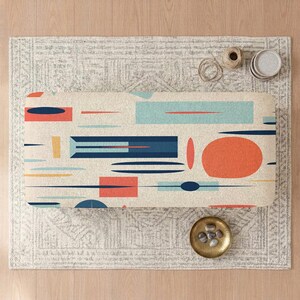 May include: A rectangular bench cushion featuring a cream-colored background with a scattered pattern of geometric shapes in navy blue, light blue, orange, and yellow, including rectangles, circles, and thin horizontal lines across the surface.