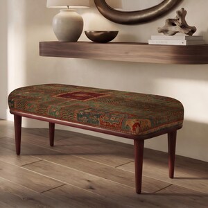 May include: A rectangular bench featuring a dark wood frame with four tapered legs and an upholstered seat covered in a multi-colored fabric with a complex, intricate pattern in shades of green, red, and brown with a central rectangular motif.