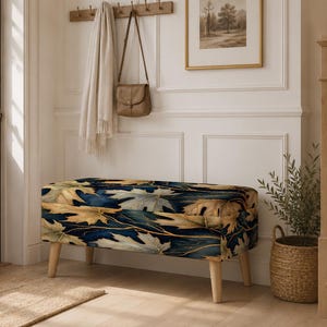 May include: A rectangular upholstered storage bench featuring a dark navy blue background with a pattern of golden and light-colored maple leaves. The bench is supported by four light-colored wooden legs and has a hinged top for storage access.