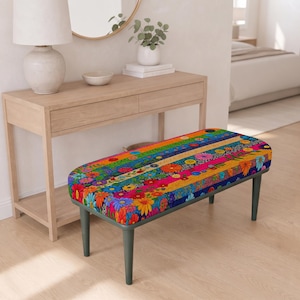 May include: A rectangular bench featuring a vibrant, multi-coloured floral pattern across its upholstered top. The fabric displays horizontal stripes of various bright colours including red, yellow, blue, and green, adorned with numerous small flower motifs. The bench is supported by four dark, tapered legs.