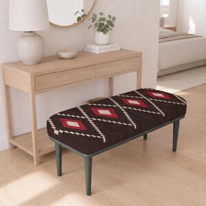 May include: A rectangular bench featuring a dark brown upholstered seat with a repeating geometric pattern of white and red diamonds. The bench is supported by four dark green tapered legs, providing a stable base for the cushioned top surface.
