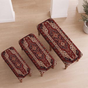 May include: Three rectangular benches of varying lengths, each featuring a top upholstered in a red, black, and cream patterned textile with geometric motifs. The benches are supported by short, turned wooden legs in a light brown finish.