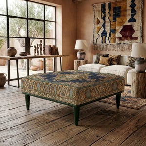 Puede incluir: Un otomano cuadrado con una cubierta de tela estampada en azul oscuro y dorado con motivos florales complejos. La base está sostenida por cuatro patas cónicas de color verde oscuro. La tapicería muestra un diseño simétrico detallado.