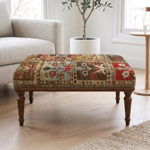 Op de afbeelding: Een rechthoekige voetenbank met een veelkleurige patchwork stoffen bovenkant met bloem- en geometrische patronen in tinten rood, blauw, geel en bruin. Het meubelstuk rust op vier donkerbruine houten poten met een gedraaid, taps toelopend ontwerp.