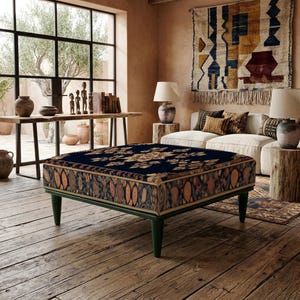 Puede incluir: Un otomán cuadrado con una parte superior azul oscuro con un patrón floral central y laterales decorados con un motivo ovalado repetitivo en tonos naranja, marrón y crema. La pieza se apoya sobre cuatro patas cónicas de color verde oscuro.