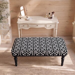 May include: A rectangular ottoman featuring a bold black and white geometric pattern on its upholstered top. The piece is supported by four dark, turned wooden legs, providing a stable base for this functional furniture item in a room setting.