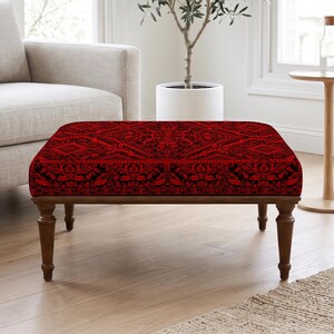 Pode incluir: Um otomano retangular com um intrincado padrão de damasco vermelho e preto no topo estofado. A peça é sustentada por quatro pernas de madeira castanho-escura com um design torneado e cónico, proporcionando uma base estável.