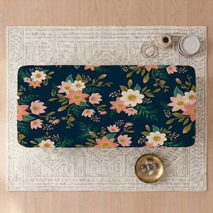 May include: A rectangular mat featuring a dark navy blue background with a repeating floral pattern of light pink and white flowers, green leaves, and thin stems. The design covers the entire surface of the mat in a dense, continuous arrangement.