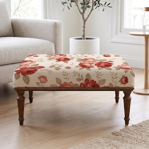 Pode incluir: Um otomano retangular com estofamento de tecido na cor creme com um padrão repetitivo de rosas vermelhas e folhas verdes. A peça é sustentada por quatro pernas de madeira marrom escura com um design torneado e acabamento liso.