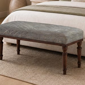 May include: A rectangular bench featuring a gray upholstered seat with a subtle white geometric line pattern. The bench is supported by four dark brown wooden legs with a turned, spindle-style design, providing a stable base for the seat.