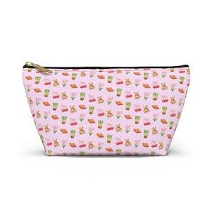 Puede incluir: Un estuche con cremallera de color rosa claro con un patrón repetitivo de pequeños osos de peluche marrones, cerezas rojas, bebidas verdes tipo matcha, tulipanes rosas y cruasanes dorados. El bolso tiene una cremallera negra en el borde superior.