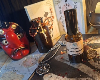 May include: A small amber glass spray bottle with a beige label reading Bayrum Protection renforcée énergétique, positioned next to a silver pendant, a red and black mask, a brown glass jar with beads, and a gold wax seal stamp.