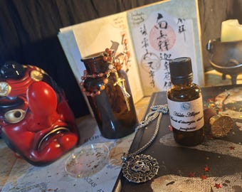 May include: A red and black Tengu mask, a brown glass bottle with a beaded necklace, a small amber glass dropper bottle with a label reading Huile Allipie, a silver skull pendant on a chain, and a gold wax seal stamp on a map surface.