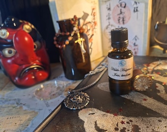 May include: A small amber glass bottle with a black cap and a white label reading "Huile Happiness Joie, bonheur". The bottle is surrounded by a red and black Tengu mask, a dark glass jar with beads, a silver pendant, and a wax seal stamp.