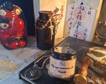 Puede incluir: Un pequeño frasco de vidrio con tapa negra y una etiqueta que dice "Riz rouge de protection" y "Expédié" se encuentra junto a un colgante de calavera de plata, un sello de cera de madera, una botella de vidrio marrón y una máscara Tengu roja.