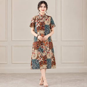 May include: A knee-length dress featuring a patchwork design with a mix of floral and paisley patterns in shades of brown, beige, blue, and red. The garment has a high mandarin collar, short sleeves, and a straight-cut silhouette that falls below the knee.