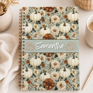 Peut inclure: Un carnet à spirales avec un motif répétitif de citrouilles blanches et de fleurs brunes et crème sur fond vert sauge. Une bande horizontale au centre affiche le prénom Samantha en écriture blanche avec deux petits dessins de citrouilles.