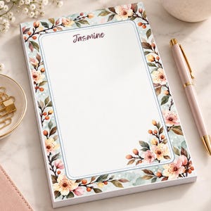 May include: A rectangular notepad featuring a white center area with the name Jasmine printed in dark script at the top. The border is decorated with a watercolor illustration of light pink cherry blossoms, green leaves, and small orange berries.