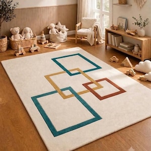 May include: A rectangular area rug featuring a cream-coloured base with a geometric pattern of interlocking squares in teal, mustard yellow, and terracotta orange. The rug has a low-pile texture and is positioned on a wooden floor in a room.