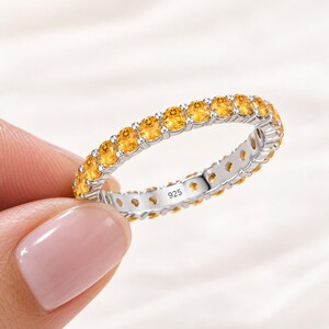 Könnte beinhalten: Ein silberner Eternity-Ring mit einer durchgehenden Reihe von runden, gelben Citrin-Edelsteinen in Krappenfassung. Die Innenseite des Metallrings ist deutlich mit dem Stempel 925 graviert, was auf eine Zusammensetzung aus Sterlingsilber hinweist.