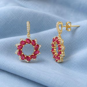 Peut inclure: Une paire de boucles d'oreilles pendantes en or avec une disposition circulaire de pierres rouges en forme de poire entourées de petites pierres transparentes. Les boucles d'oreilles ont un fermoir à tige et un maillon de chaîne en or.