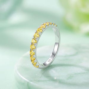 Peut inclure: Une bague en argent sterling ornée d'une rangée de pierres précieuses jaunes taillées en rond sur la moitié supérieure. L'intérieur de l'anneau porte la gravure 925, indiquant la teneur en argent de ce bijou.
