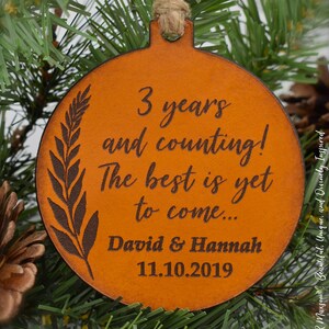 May include: A brown leather ornament with the text "3 years and counting! The best is yet to come... David & Hannah 11.10.2019" engraved on it.