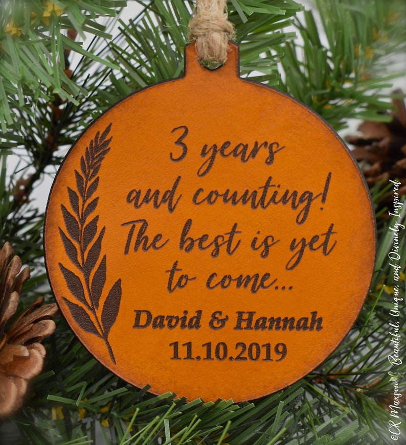 May include: A brown leather ornament with the text "3 years and counting! The best is yet to come... David & Hannah 11.10.2019" engraved on it.