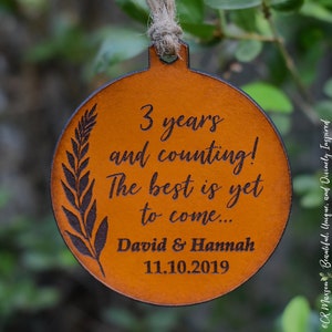 May include: A brown leather ornament with the text "3 years and counting! The best is yet to come... David & Hannah 11.10.2019" engraved on it.