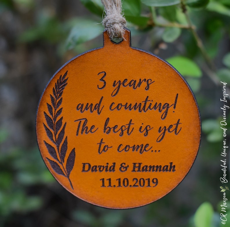 May include: A brown leather ornament with the text "3 years and counting! The best is yet to come... David & Hannah 11.10.2019" engraved on it.