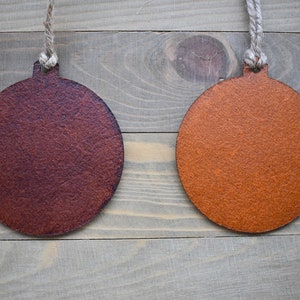May include: Two round, wooden ornaments hanging from twine against a woodgrain background. The ornament on the left is a dark brown color, while the ornament on the right is a light orange color.