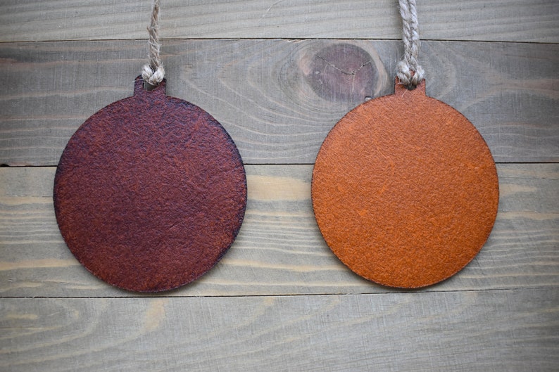 May include: Two round, wooden ornaments hanging from twine against a woodgrain background. The ornament on the left is a dark brown color, while the ornament on the right is a light orange color.