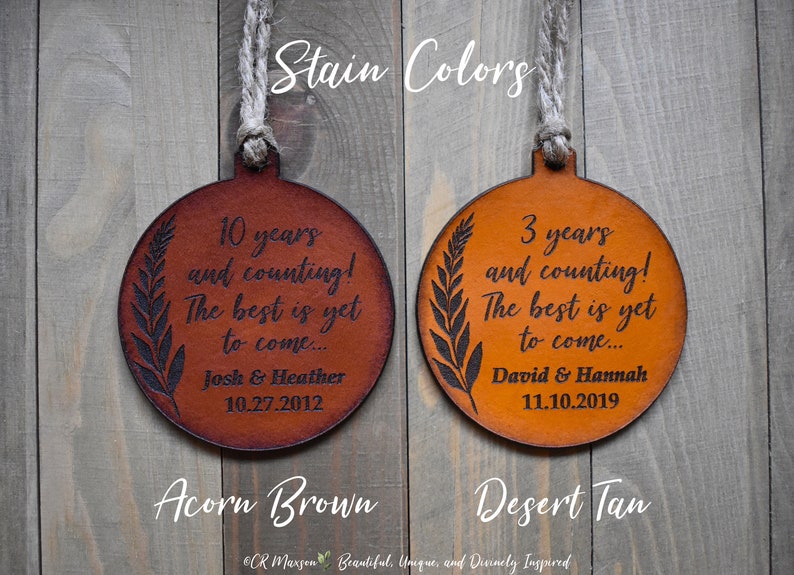 May include: Two leather ornaments with a leaf design and personalized text. The ornament on the left is acorn brown and says "10 years and counting! The best is yet to come... Josh & Heather 10.27.2012". The ornament on the right is desert tan and says "3 years and counting! The best is yet to come... David & Hannah 11.10.2019".