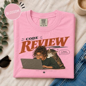 Könnte beinhalten: Ein rosafarbenes T-Shirt mit Rundhalsausschnitt und einer Grafik einer Person mit Brille am Laptop, auf deren Schulter eine getigerte Katze sitzt. Der Text lautet CODE REVIEW und I have concerns. Das Shirt hat ein Comfort Colors Etikett in XL.