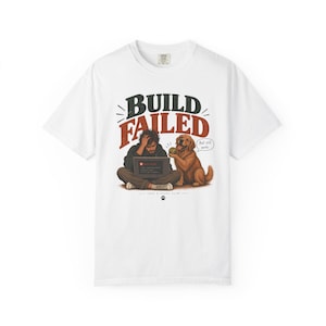 Puede incluir: Una camiseta blanca de manga corta con un gráfico de una persona sentada con un portátil y un perro golden retriever. El texto BUILD FAILED aparece sobre la persona y Ball still works en un bocadillo. Hay una huella en la parte inferior.