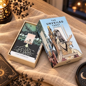 May include: The Unveiled Tarot deck by Jesse Lonergan in a light blue box with a graphic illustration of a figure holding a sword. Beside the box, an open card from the deck displays The Empress, featuring a tree root design and a small figure.