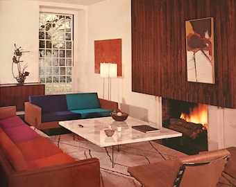 May include: A living room featuring a white marble coffee table, a tan leather chair, and two sofas with multi-coloured cushions in blue, teal, purple, and orange. A fireplace with a burning fire is set into a dark wood panelled wall with art.
