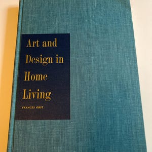 以下が含まれることがあります： 「Art and Design in Home Living」というタイトルが金色で、紺色の長方形のラベルに書かれた、ターコイズ色のハードカバーの本。著者の名前、Frances Obstはタイトルの下に印刷されています。